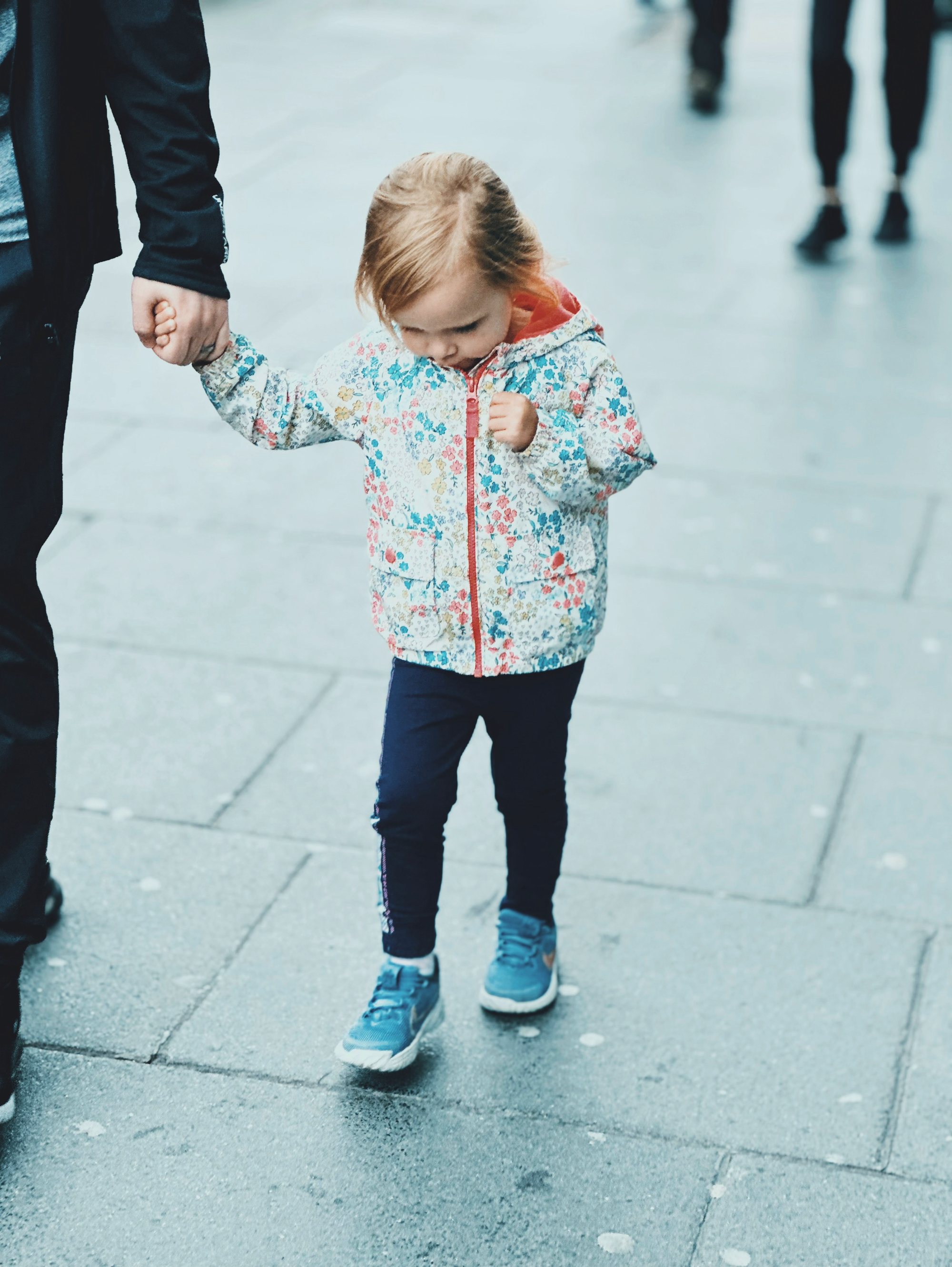 A small child holding an adult’s hand on a city street